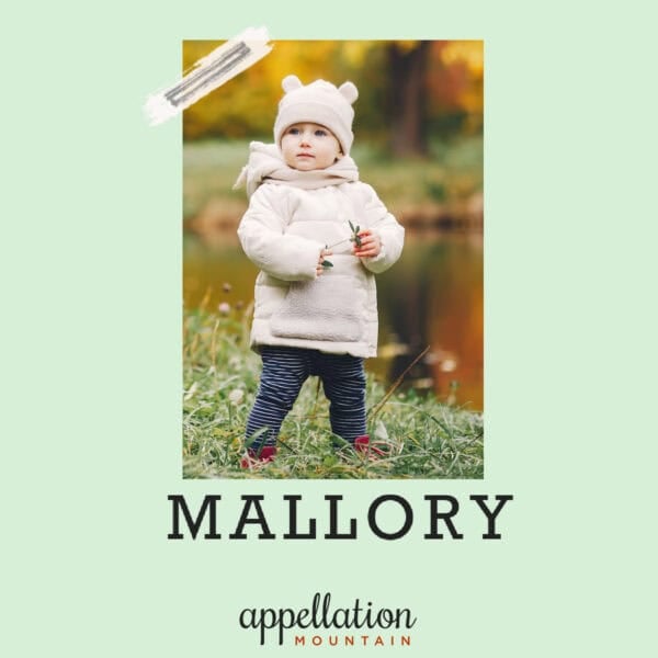Young child standing outdoors in a cream puffer coat with a hat, by a lake in autumn.