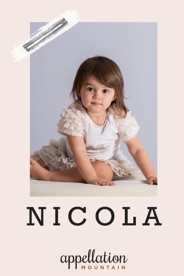 toddler girl with brown hair wearing white and gray dress looking at camera; baby name Nicola