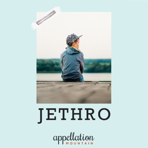 boy sitting on dock looking at lake wearing blue jacket and baseball cap; baby name Jethro