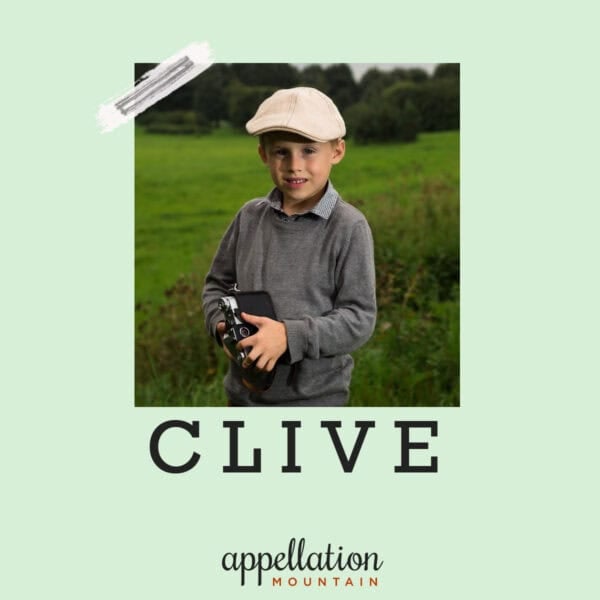 boy child wearing a sweater and a beige newboy's cap standing outside with a camera; baby name Clive