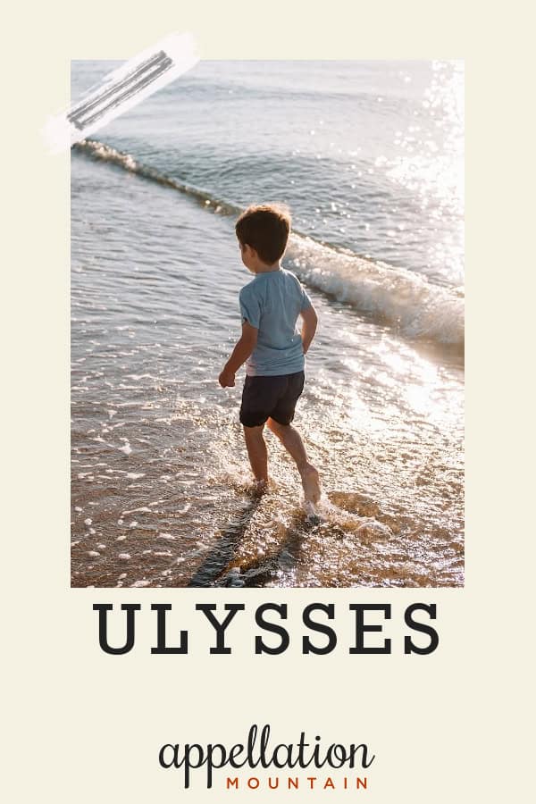 blonde toddler boy walking at on beach at ocean's edge wearing shorts and tee shirt; baby name Ulysses