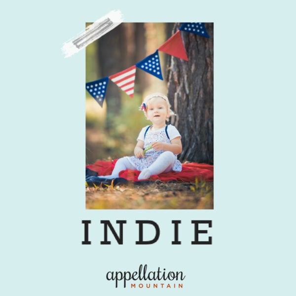 blonde girl child sitting under red white and blue bunting next to tree; baby name Indie
