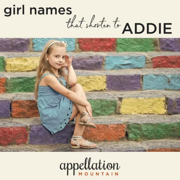 young girl with blonde hair in blue dress sitting against colorful painted brick wall "Addie names"
