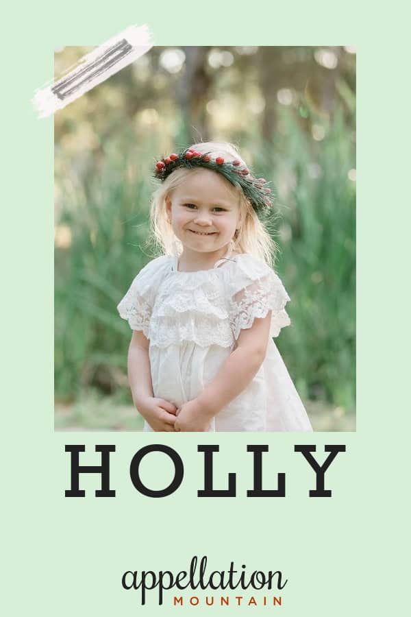 girl child wearing white dress and wreath of holly standing outside in a field; baby name Holly