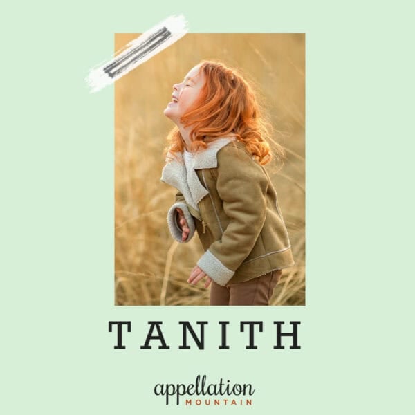 girl child with auburn hair wearing shearling jacket standing in field of golden grass; baby name Tanith