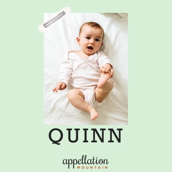 baby lying on back, holding one foot, wearing light yellow snapsuit; baby name Quinn