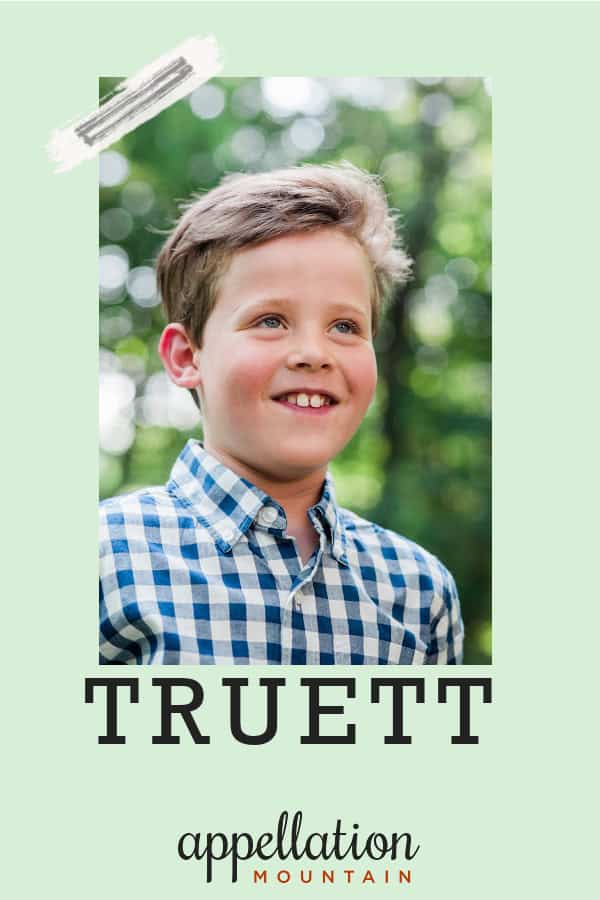 blonde boy child wearing button-up plaid shirt standing outside with trees in background; baby name Truett