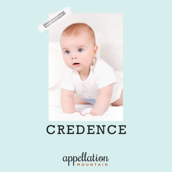 baby boy with light red-brown hair and blue eyes wearing white onesie kneeling on white sheet; baby name Credence