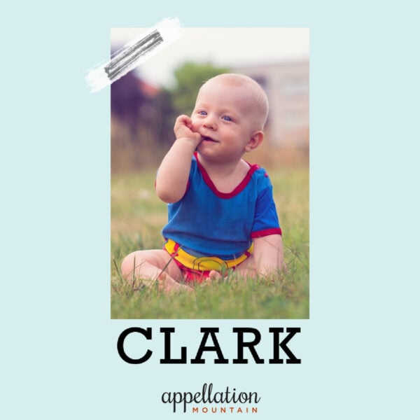 blonde baby boy sitting in field wearing superhero style onesie; baby name Clark