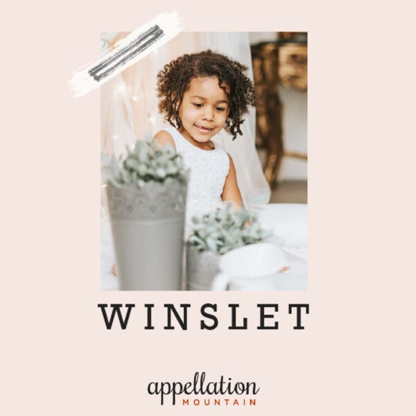 girl with dark curls wearing white dress seated behind potted plants; "baby name Winslet"