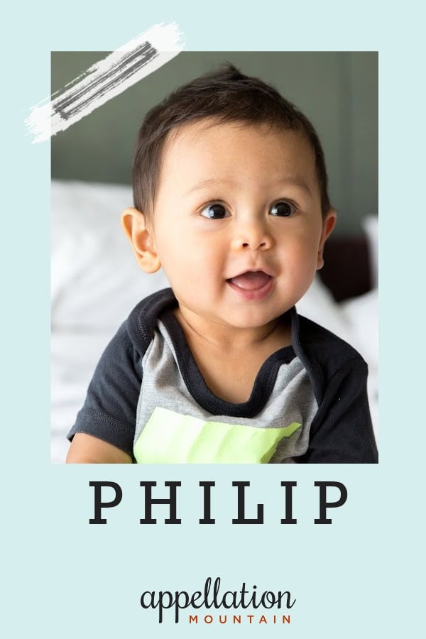Asian baby boy wearing gray and blue shirt with happy expression on white bed; baby name Philip