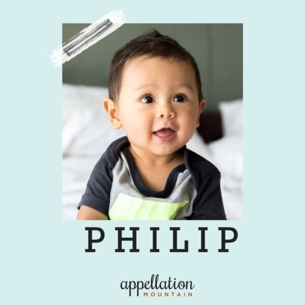 Asian baby boy wearing gray and blue shirt with happy expression on white bed; baby name Philip