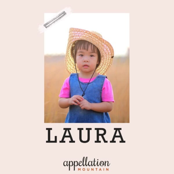 girl of Asian descent wearing straw hat and denim jumper standing in field; baby name Laura