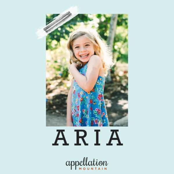 girl child with long blonde hair wearing blue floral sundress standing outside in garden; baby name Aria