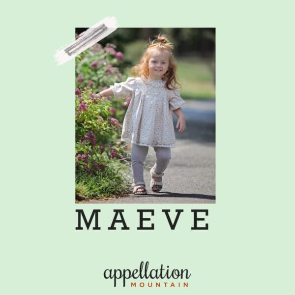 girl child with reddish hair wearing floral dress walking in lane with floral shrubs; baby name Maeve