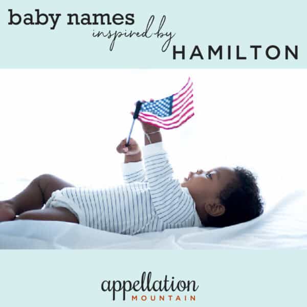 black baby boy wearing striped onesie holding American flag; baby names inspired by Hamilton