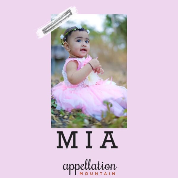 girl of Indian descent wearing pale lavender fancy dress sitting in field; baby name Mia