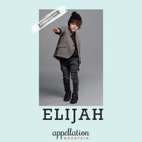 boy child wearing knit cap, blazer, dark jeans, pointing at camera; baby name Elijah