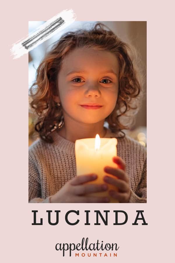 girl with wavy blonde hair wearing a light pink sweater holding a lit candle; baby name Lucinda