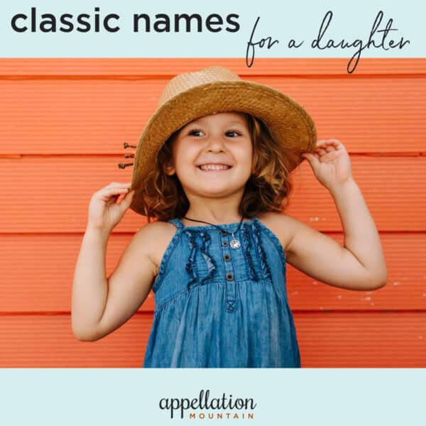 young girl with curly brown hair wearing woven sun hat and denim jumper against orange siding background; classic girl names