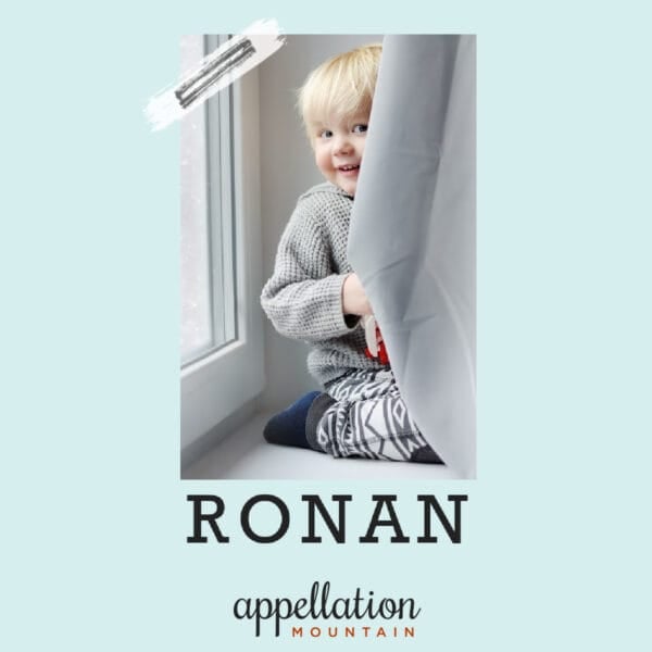 blonde toddler boy peeking out behind gray curtain; baby name Ronan