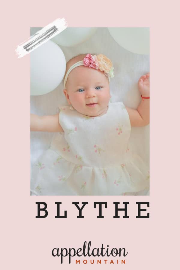 happy baby girl wearing white dress and headband with pink flowers on white background with white balloons; baby name Blythe
