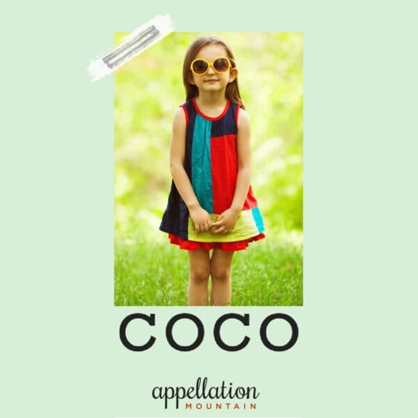 girl child wearing color blocked dress and big sunglasses standing outdoors in field; baby name Coco