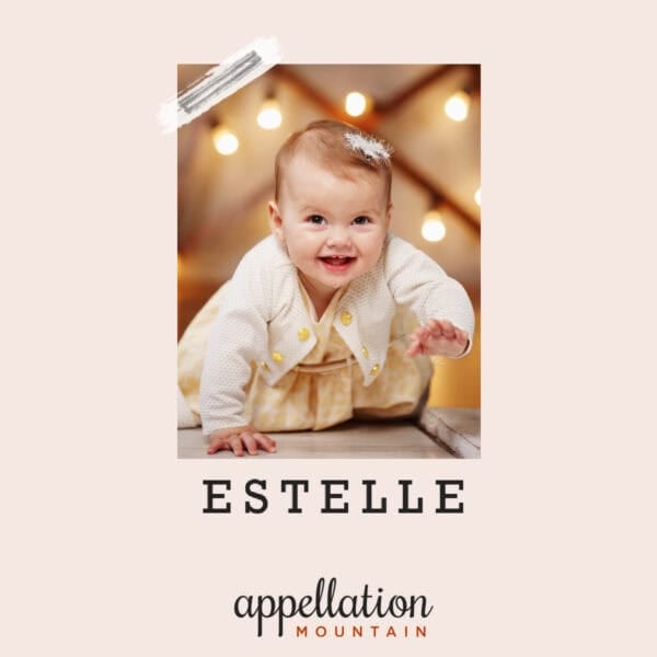 baby girl with light brown hair wearing off white sweater with string lights behind her; baby name Estelle