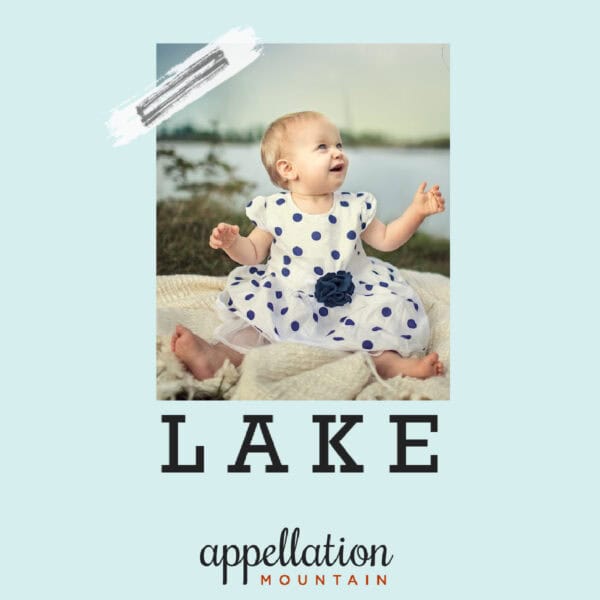 baby girl in white and blue polka dotted dress, sitting in front of a lake