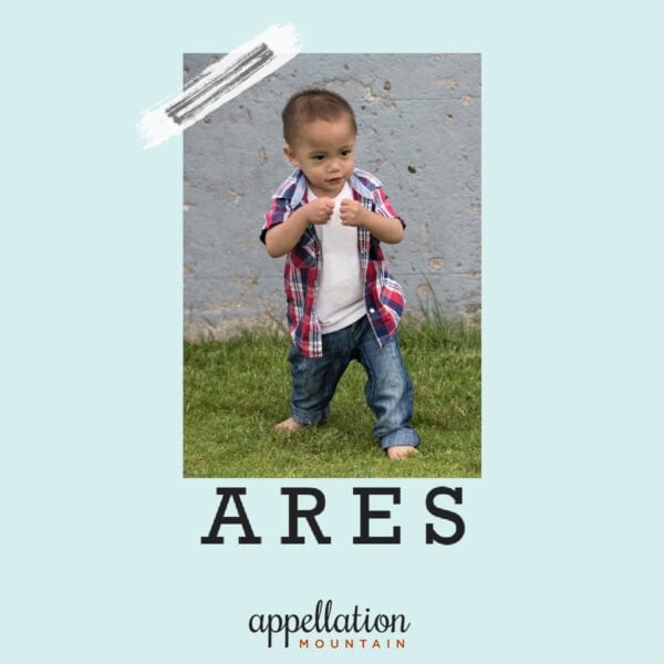 toddler boy with dark curls wearing jeans and plaid shirt with his fists up "baby name Ares"