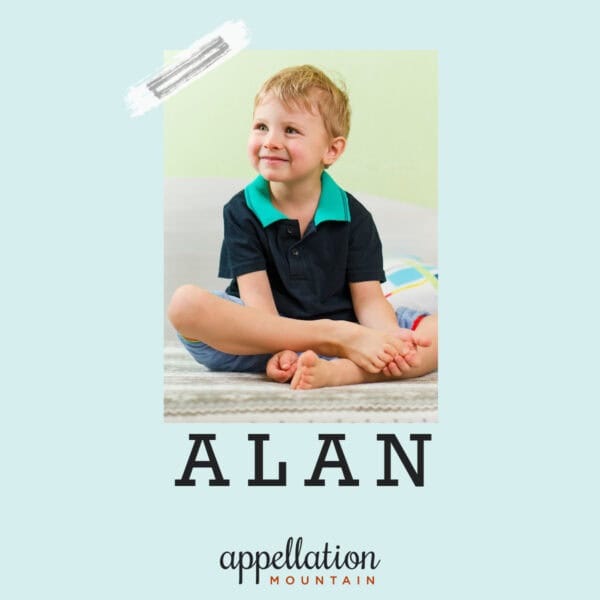 young boy with blonde hair wearing green collar shirt and blue pull over, sitting with legs crossed; baby name Alan