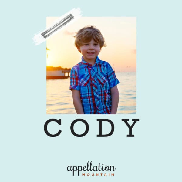 young boy in blue plaid shirt standing with sunset over water as a backdrop; baby name Cody