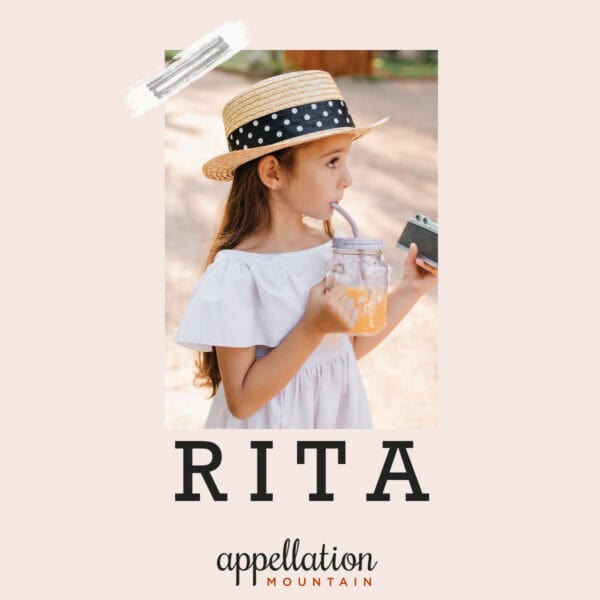 young girl wearing straw hat with polka dot ribbon and white dress, drinking from a glass, holding a camera in her other hand, baby name Rita