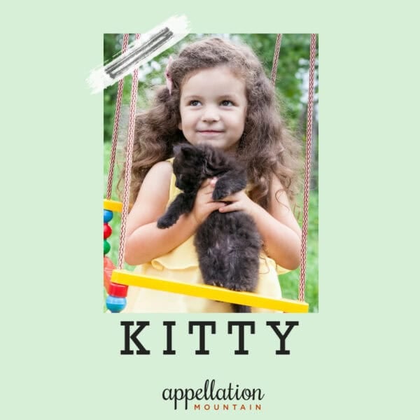 girl child with long wavy brown hair wearing yellow sundress holding black cat; baby name Kitty