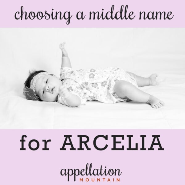 baby girl with dark hair wearing headband and floral print onesie lying on her back with one arm reaching up; middle name for Arcelia