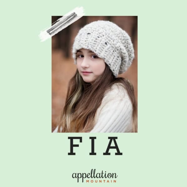 girl child with long dark hair outside wearing ivory knit hat and sweater; baby name Fia