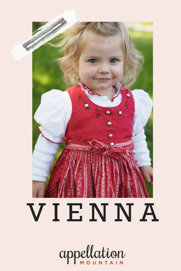 blonde toddler girl in traditional red dress with white puffed sleeve top; baby name Vienna