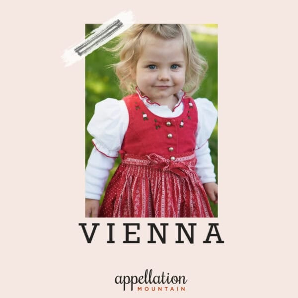 blonde toddler girl in traditional red dress with white puffed sleeve top; baby name Vienna