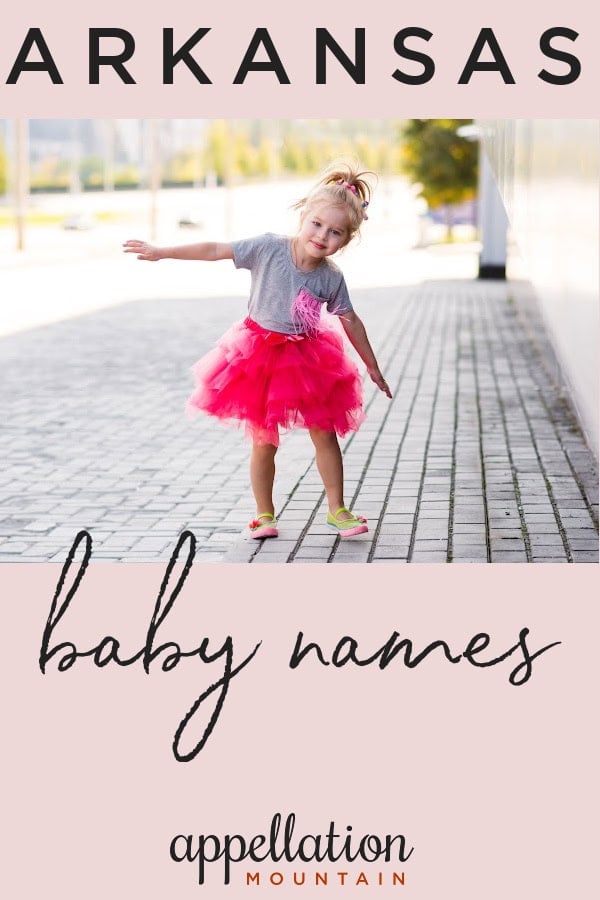 girl child in bright pink skirt and striped top standing on deck outside in front of lake and trees; Arkansas baby names