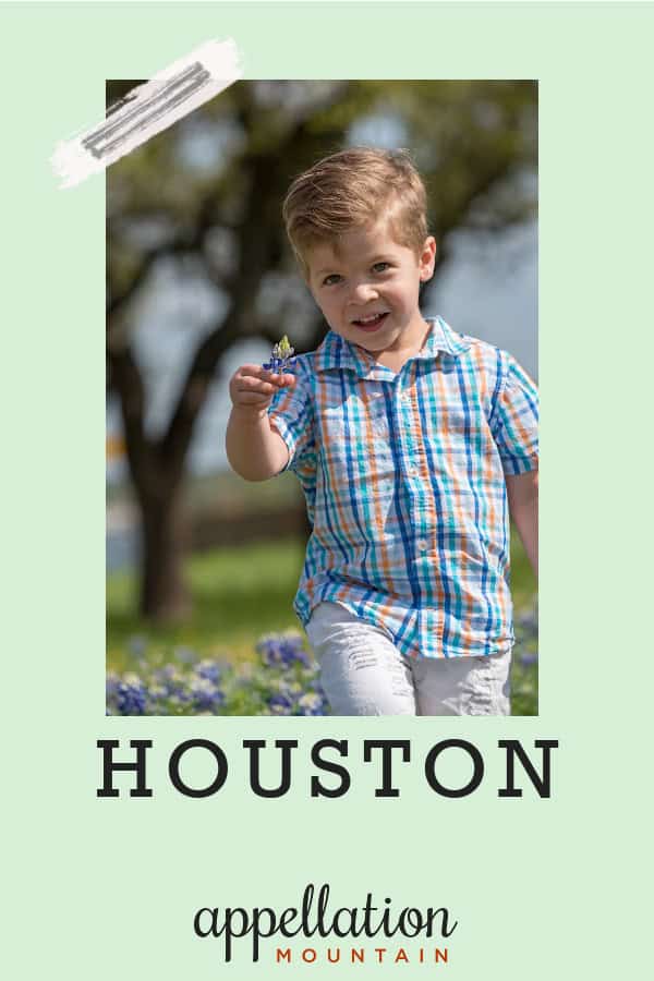 blonde boy child wearing blue plaid shirt, pointing toward camera while walking across field with tree in background; baby name Houston